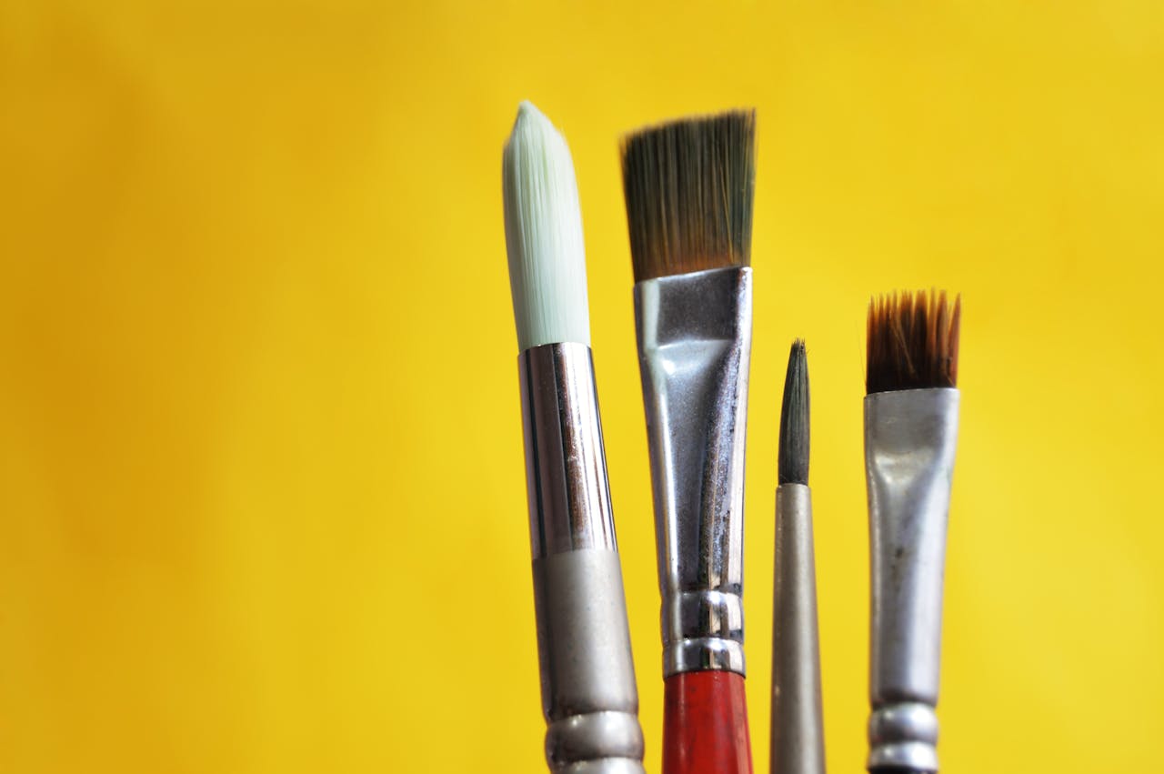 Close-up of varied paint brushes against a bright yellow backdrop.
