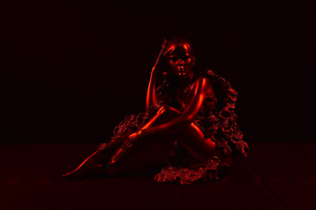 Sculptural portrait of a woman in dramatic red lighting with a dark background.