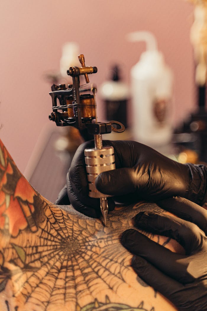A tattoo artist working on a spiderweb design using a tattoo machine.